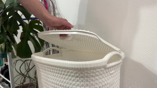 A person lifts the lid of a dirty laundry basket and then lets it fall, portraying a cleaning or tidying action