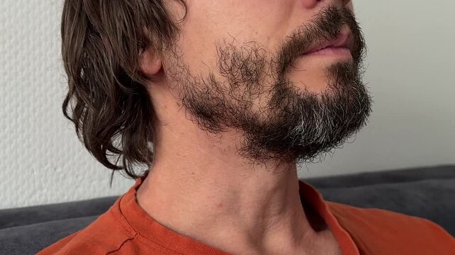 Man in side profile with neutral expression and steady gaze. Beard, mustache, and jawline visible. Calm, observant moment in indoor scene