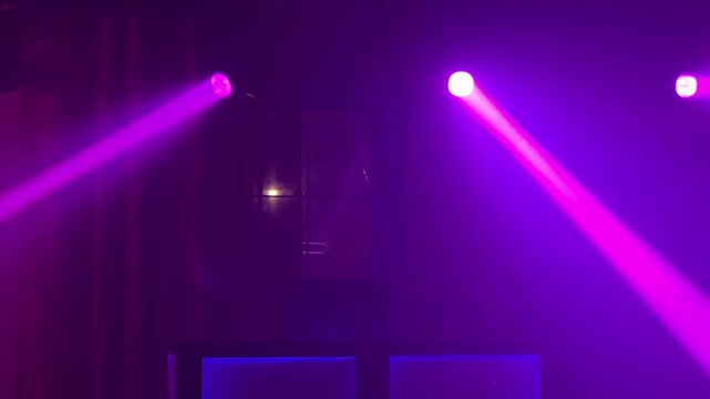 Vibrant magenta and purple stage lights sweeping through thick theatrical fog. Silhouette of stage equipment is visible in the energetic club.