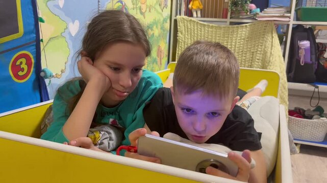 Two children boy and girl, play games or watch informational video text on Internet on mobile phones and tablet computers at home on sofa. Leisure, children, digital technology and people concept