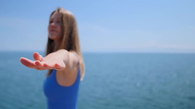 woman performing warrior ii yoga pose rear side view while camera pan left on wooden pier by lake, outdoor fitness training near water, balance strength and controlled movement during workout session