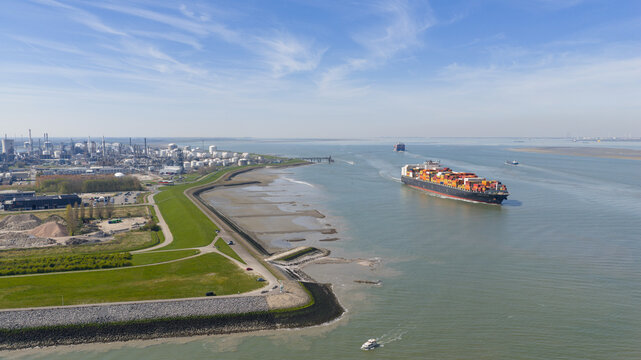 Hoek, Netherlands: Aerial view of the Dow Chemical industrial complex and a large container ship on the Westerschelde river under a blue sky.