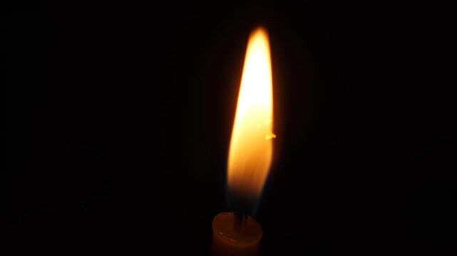 Macro shot of a bright candle flame on an isolated black background. Detailed view of a burning wax candle wick in complete darkness
