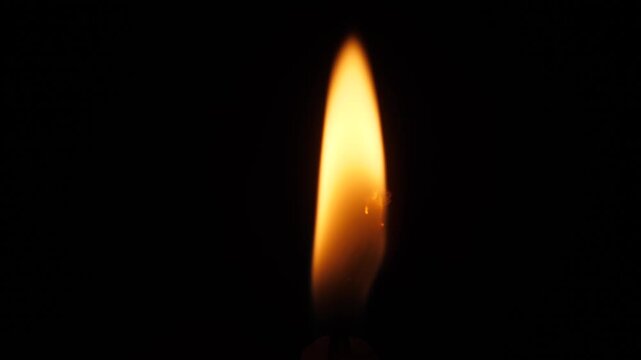 Close-up of a wax candle flame burning in complete darkness. A solitary light source illuminating the gloom