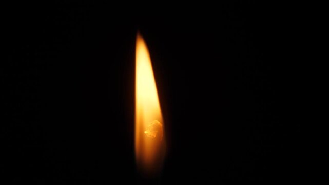 Macro shot of a candle flame flickering against a deep black background. The bright fire of the wick creates an atmosphere of peace and tranquility