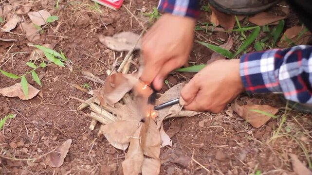 Close up of hands using ferro rod to light a fire with dry leaves in the forest, bushcraft survival skill.