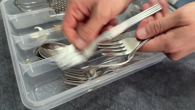 A person organizing silver forks in a cutlery tray
