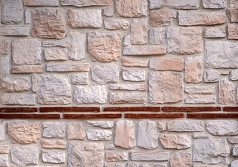Fototapeta premium Stone wall texture with mixed natural rocks and brick detail. Rustic masonry background with neutral tones for architectural and design use. Rich texture, varied sizes.