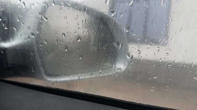Car side mirror seen through wet window with rain drops