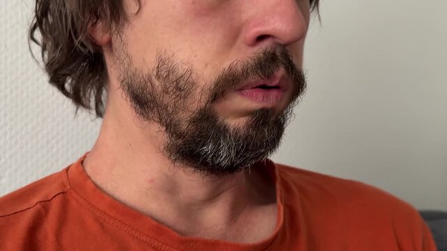Man coughs with closed eyes and visible throat tension. Beard and mustache visible. Indoor close-up gesture tied to discomfort, illness, or reflex