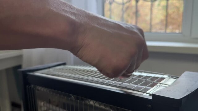Fingers gently slide across the grill of an electric heater