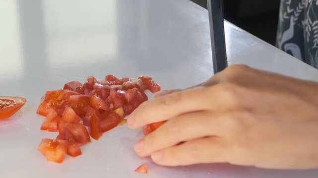 woman hands cutting tomato close-up finely dicing on cutting board, kitchen food preparation process with knife, fresh vegetable handling for cooking meals and healthy recipes