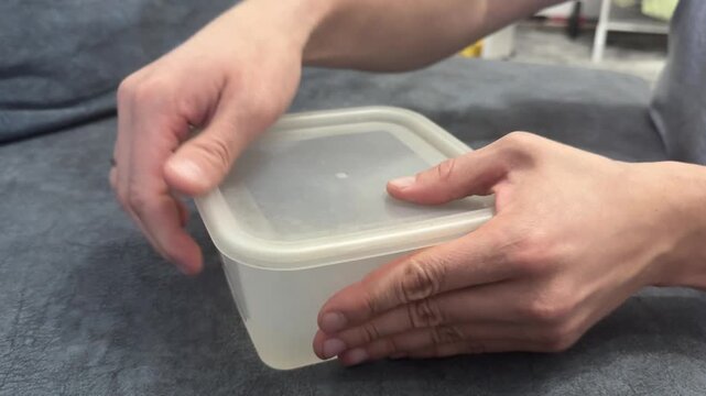 Hands closing lid of a plastic food container. Home kitchen organization or meal storage concept. Focus on sealing and daily household routine