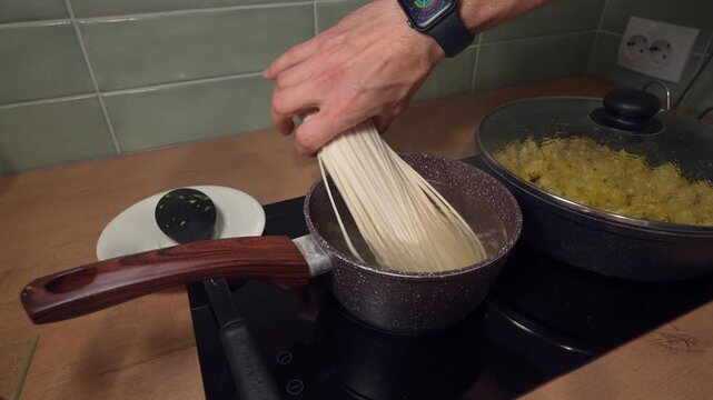male hands adding pasta into boiling pot close-up, kitchen cooking process with placing long noodles into hot water, preparing meal, action of lowering spaghetti into saucepan on stovetop