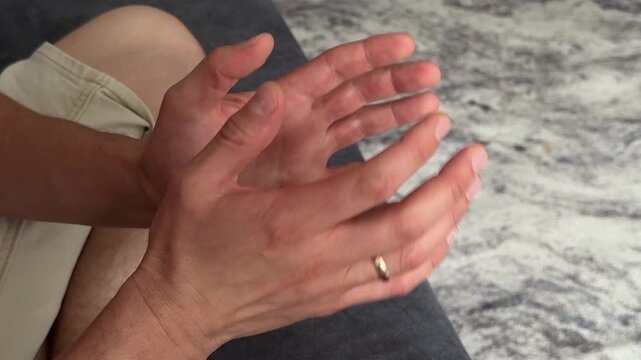 Man taps the knuckles of his fingers together in a rhythmic, repetitive motion. Gesture suggesting restlessness, focus, or habit. Close-up view of hands in calm setting.