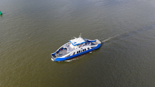 Amsterdam, Netherlands - 14 April 2026: Aerial view of a blue and white ferry boat cruising across the IJ water near Zeeburgereiland with passengers visible on the deck.