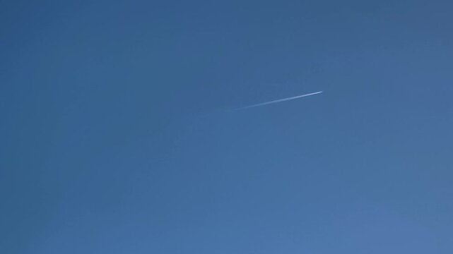 Commercial airplane flying at high altitude leaving a white condensation trail against a vivid blue sky. Air travel and transportation concept