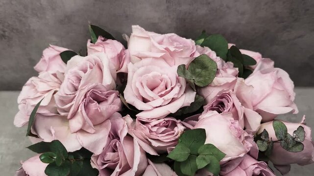 Beautiful bouquet of dusty pink roses with eucalyptus leaves rotating on a gray textured background. Romantic floral arrangement for weddings