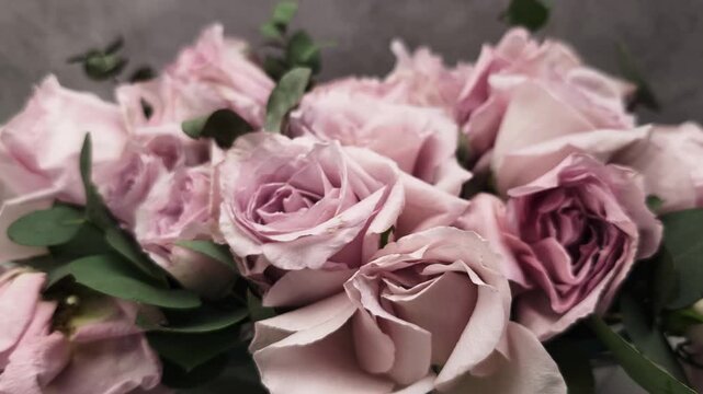 Wilting bouquet of pink and purple roses with green leaves in a glass vase dying against a gray background. A concept of aging and time
