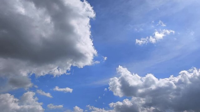 Majestic white and gray cumulus clouds moving gracefully across a beautiful bright blue sky. The sun shines brightly, creating a serene and scenic skyscape