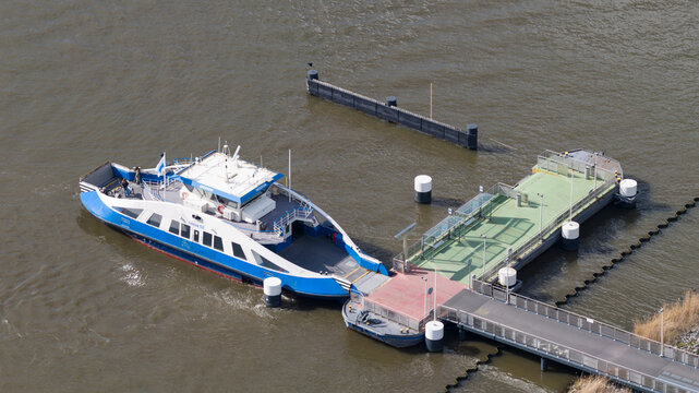 Amsterdam, Netherlands - 14 April 2026: Aerial view of a blue and white GVB ferry docked at the Zeeburgereiland pier with mooring bollards and murky water.