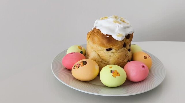 Sweet easter bread, also known as kulich or paska, rotating on a plate surrounded by colorful decorated eggs on a white background