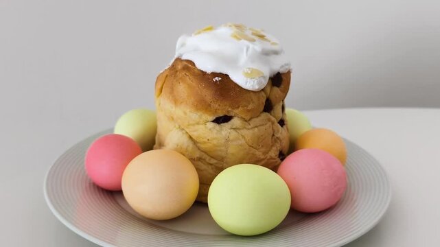 Delicious easter cake with white icing and almond flakes, surrounded by colorful painted eggs. The traditional holiday dessert rotates on a plate