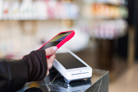 Digital Wallet Tech. Person using NFC technology to complete a transaction in a boutique. Pink mobile phone making a contactless connection with a sleek electronic payment device.