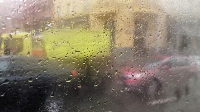 Rainy weather view from a car window. Water drops sliding down the glass with blurred city street traffic and colorful lights in the background