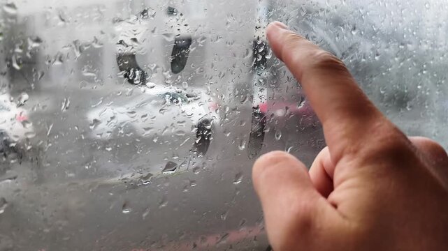 Close up of a person finger writing the word spring on a misted window with raindrops, revealing a blurry street view outside