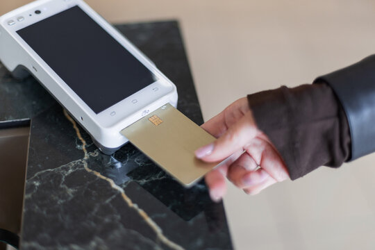 Close-up of a hand inserting a gold credit card into a white terminal for a chip-and-pin transaction. Concept of secure payment, retail checkout, and financial technology in a modern shop.