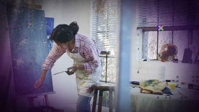 Painter reaching to canvas scraping lower edge with brush texturing while purple overlaying studio
