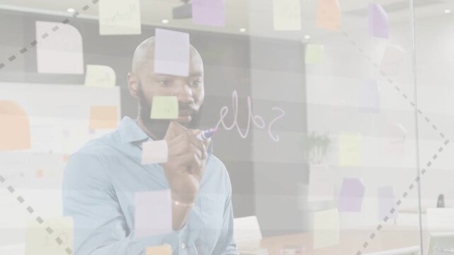 Facilitator responding to business prompt, marking clear glass with marker while reviewing stickies
