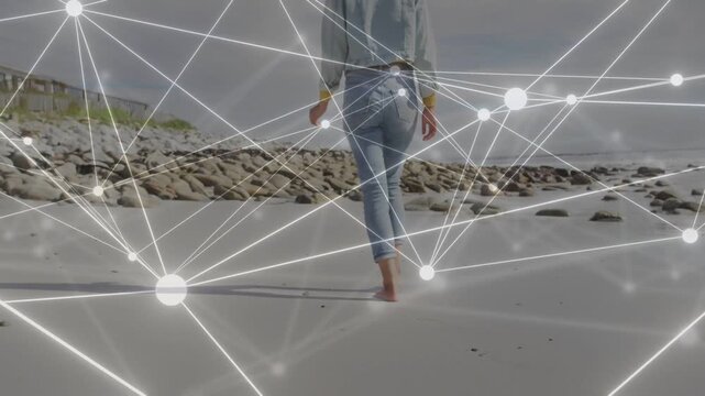 Woman walking along sandy shore, barefoot steps activating glowing node network, showing tech demo