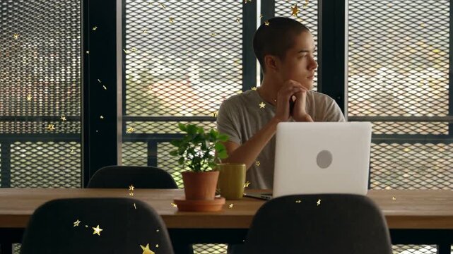 Man starting laptop work, clasping chin, glancing at mesh window while gold stars drifting in front