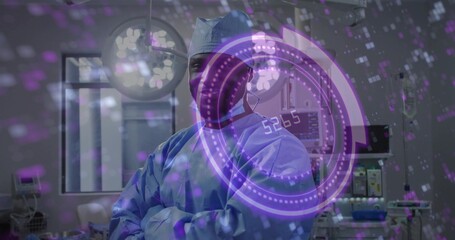 Obraz premium Standing adult surgeon wearing blue scrubs and cap in operating room, with vital monitor and HUD