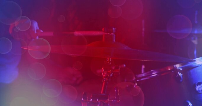 Glowing crash cymbal catching stage lights at club, showing stand hardware and drummer in dark gear