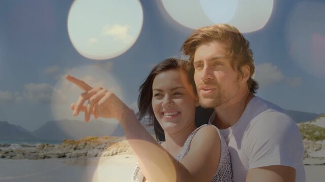 Woman pointing, man embracing and speaking, bokeh overlay fading, revealing shoreline for marketing