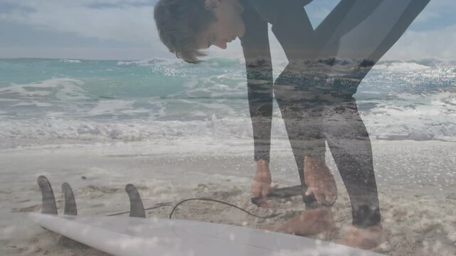 Male surfer bending and fastening ankle leash by surfboard, grabbing cord, preparing for surfing