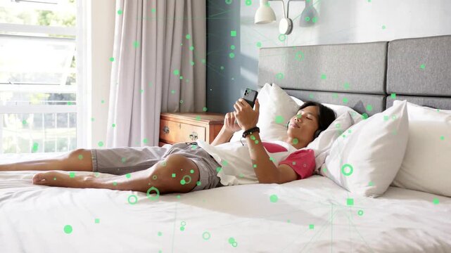 Teen boy on bed tapping phone, scrolling, lowering it to chest, dozing under tech overlay floating