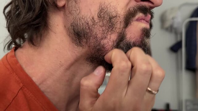 Man scratching his beard with knuckles in a thoughtful or irritated gesture. The movement emphasizes facial hair texture and natural grooming habits