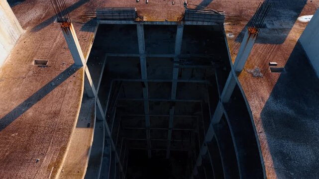 High angle view looking down into concrete building shaft. Looking down from a high floor into the central void or elevator shaft of an unfinished concrete building.