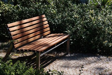 Obraz premium A simple wooden bench sits on a paved path, surrounded by greenery.