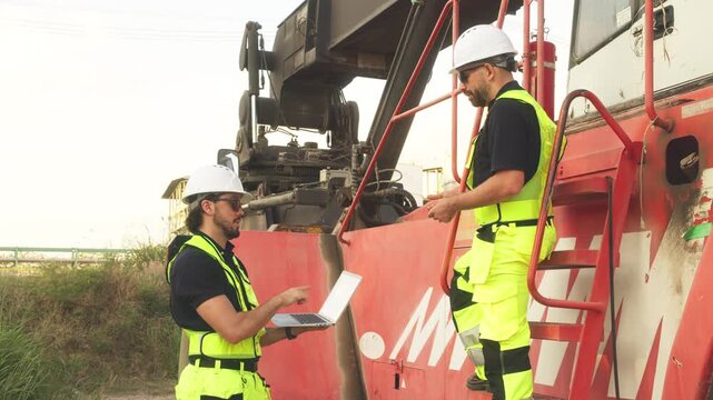 Two engineers in safety vests analyze laptop data near cargo truck and container, coordinating logistics and industrial transport operations.