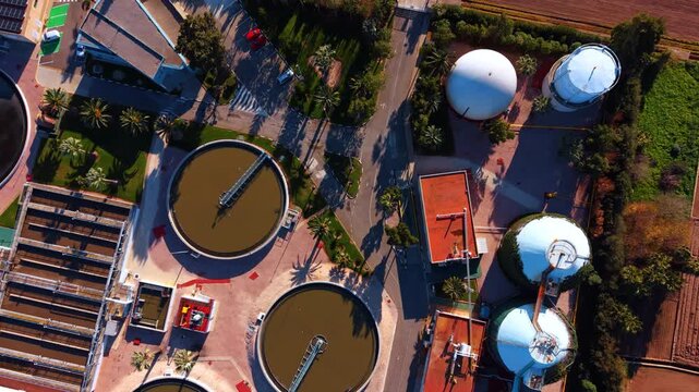 Aerial top down view of circular tanks and silos. Vertical top view of wastewater treatment facility with circular sedimentation pools and white storage silos.