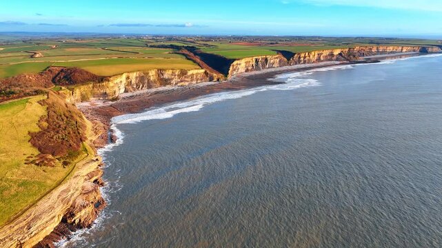 Aerial view of Southerndown coastline with limestone cliffs and fields. Drone perspective of the Heritage Coast cliffs and green agricultural land in Dunraven Bay, South Wales, UK.