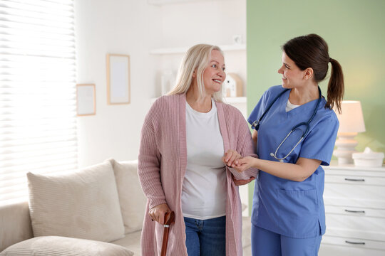 Smiling care worker supporting senior woman with walking cane at nursing home. Space for text