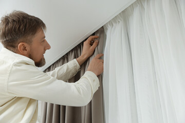 Man hanging window curtain in room, low angle view. Space for text © New Africa