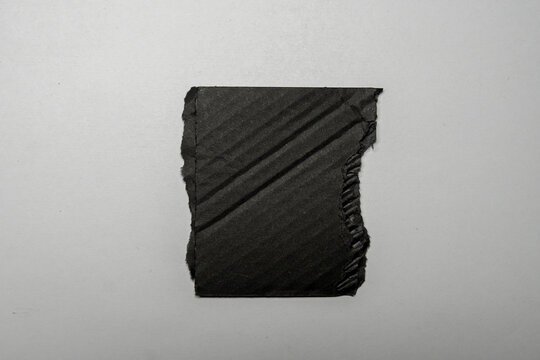 A piece of black paper showing a crisp texture and ripped edges, placed on a white background. This visual element can be used for creative projects, advertising, or art concepts.