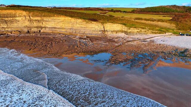 Aerial view of wave-cut platform and tide pools at Southerndown. Downward drone shot of rocky beach formations, tide pools, and limestone strata at Dunraven Bay beach.